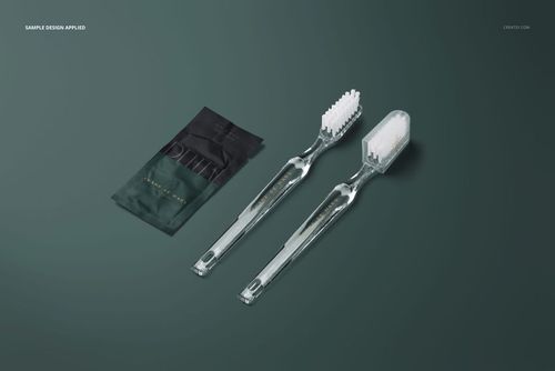 Clear toothbrushes and a compact toothpaste sachet displayed on a dark green surface in a hotel dental kit mockup.