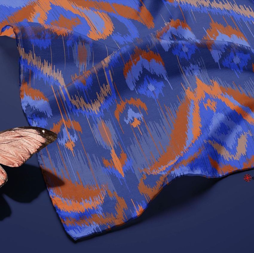 Habotai silk scarf mockup featuring a blue and orange ethnic motif pattern, shown draped on a dark blue surface with a butterfly prop.