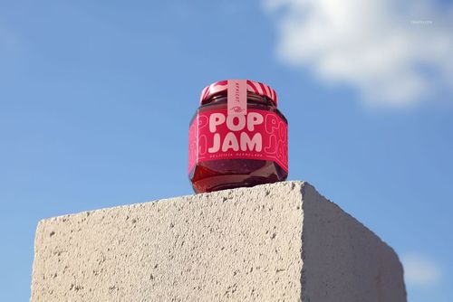 Front-facing jam jar mockup featuring a vibrant pink label, set atop a textured concrete surface under a clear sky.