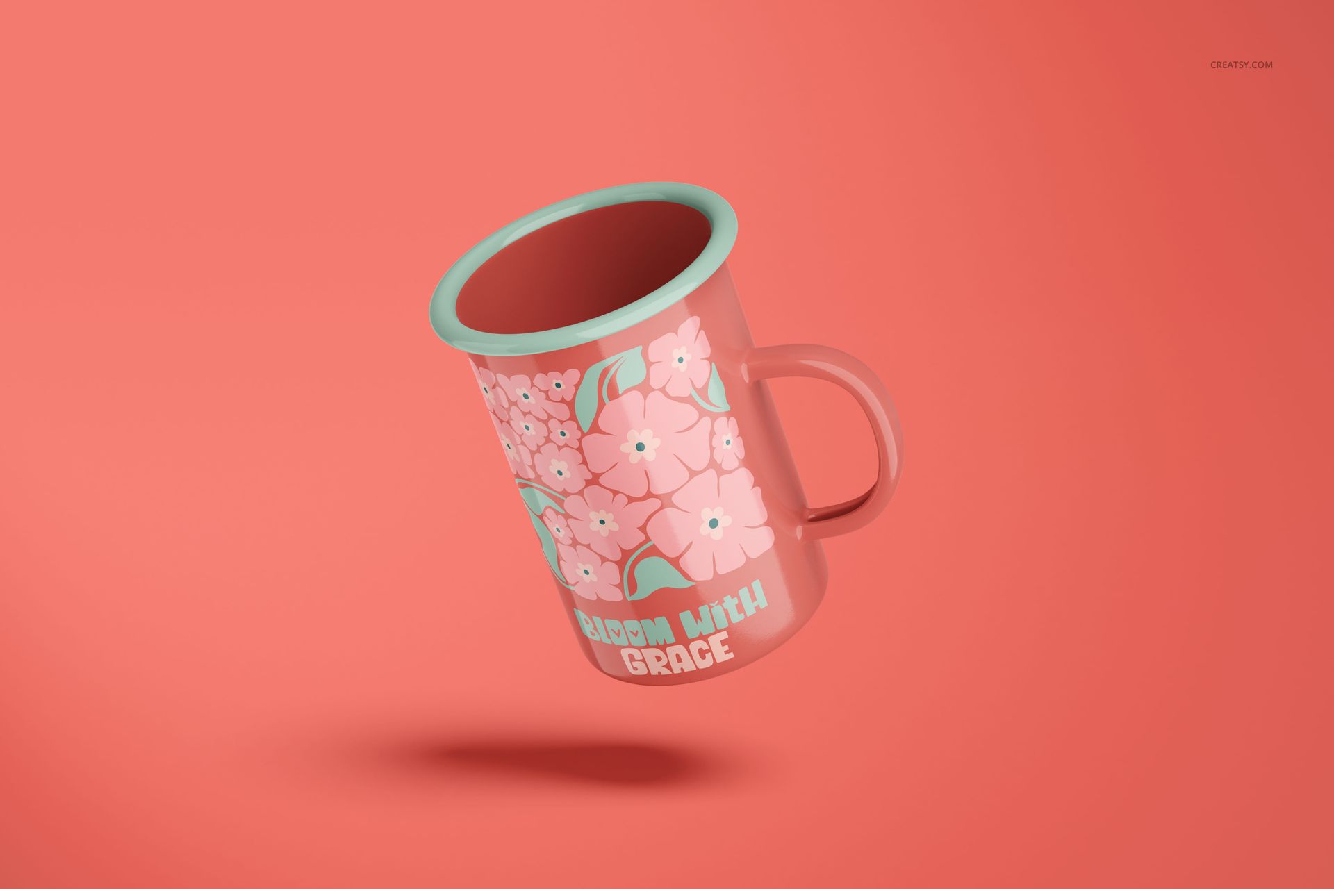 Enamel mug mockup with pink body, mint accents, flower design, and lettering, shown at an angle on coral backdrop.