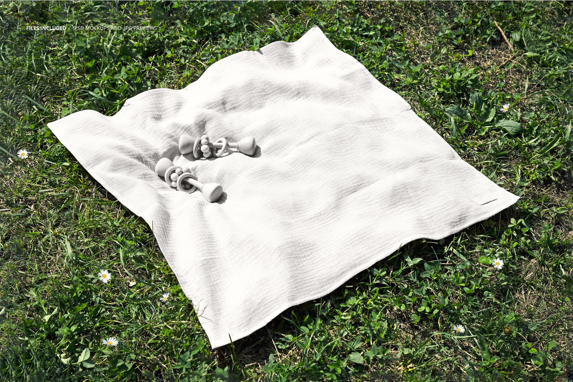 Top view of a crinkle cotton muslin swaddle blanket mockup laid out on grass with two baby rattles on top.