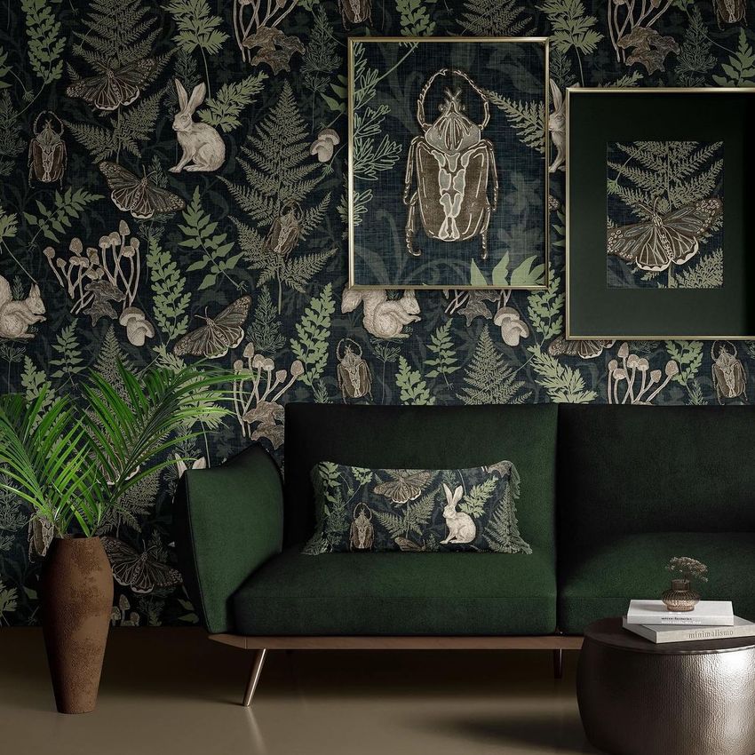 Interior scene mockup showing a dark green sofa with a botanical pillow, leafy plant, and nature-themed framed posters on a patterned wall.