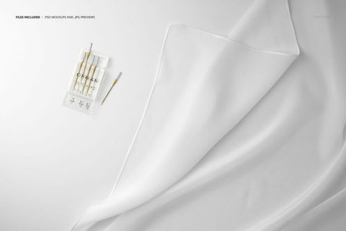 Close-up view of a white silk scarf mockup draped on a flat surface with sewing needles placed nearby.