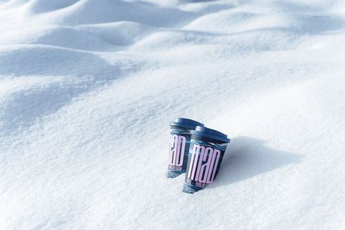 PSD mockup of two drinkware paper cups with colorful graphic design, positioned on snowy ground with soft shadows.