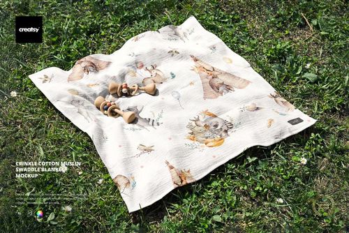 Top view of a crinkled muslin swaddle blanket mockup featuring playful animal designs and wooden rattles outdoors.