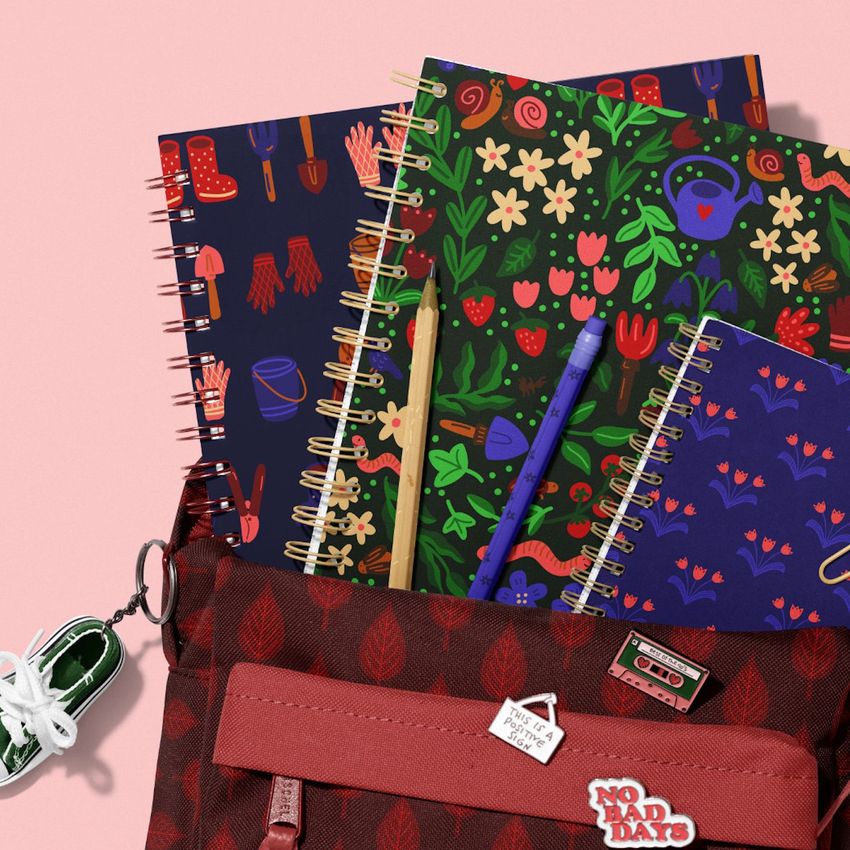 School backpack mockup with spiral notebooks featuring colorful gardening-themed covers, pens, and a sneaker keychain on a pink background.