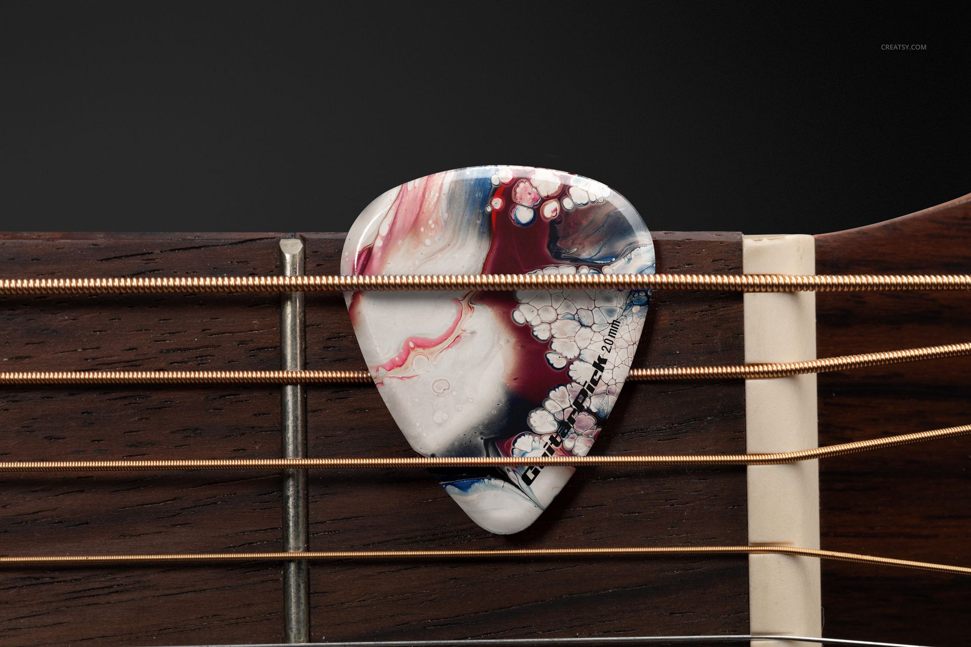 Detailed PSD mockup showing a multicolored guitar pick placed under metal strings on a wooden guitar fretboard, front angle.
