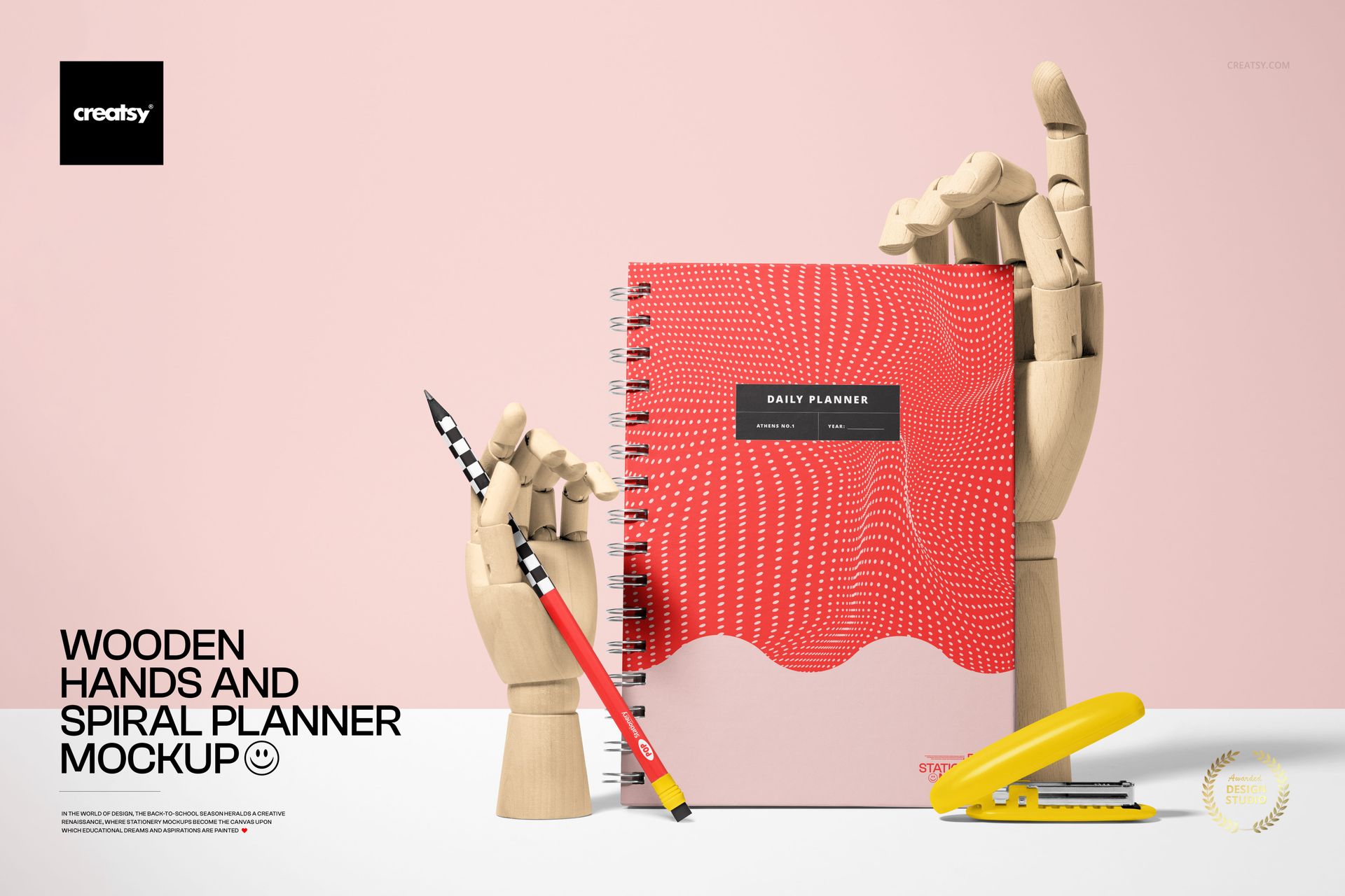 PSD mockup showing a spiral planner with geometric red cover, wooden hands, a yellow stapler, and a pencil on a pink background.