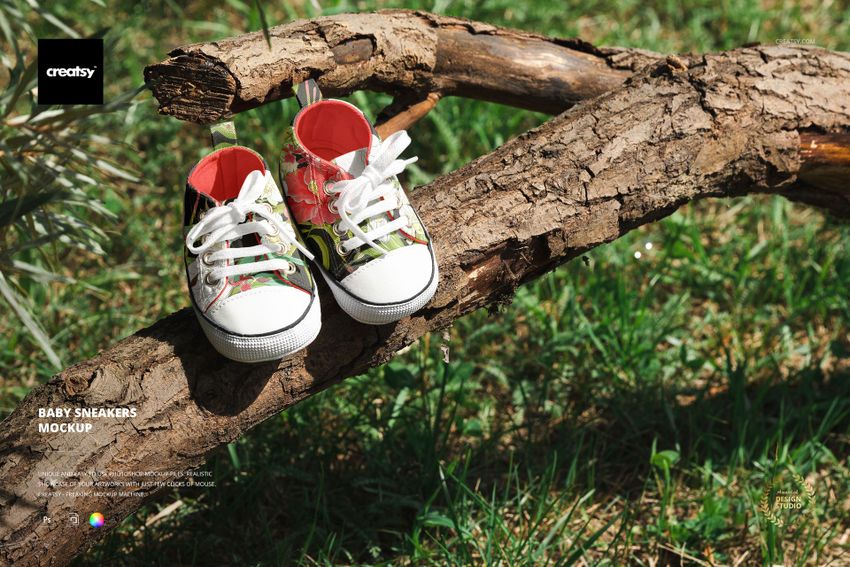Baby sneakers mockup featuring two shoes with multicolored designs, white soles, and laces, placed on a log outdoors.