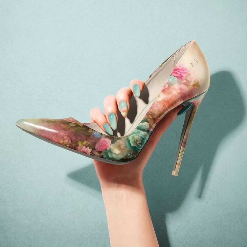 High heels mockup featuring a hand holding a pointed stiletto shoe with a pastel floral pattern, set against a teal background.