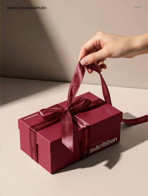 Luxury gift box mockup with burgundy ribbon and box, viewed from a front angle on a beige background.