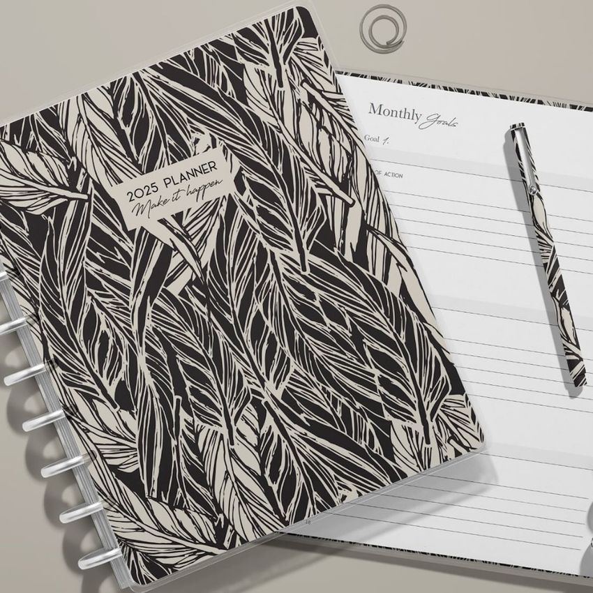 Flat lay of spiral planner mockup with abstract leaf cover, open to a lined goals page, pen and paperclip on a neutral desk.