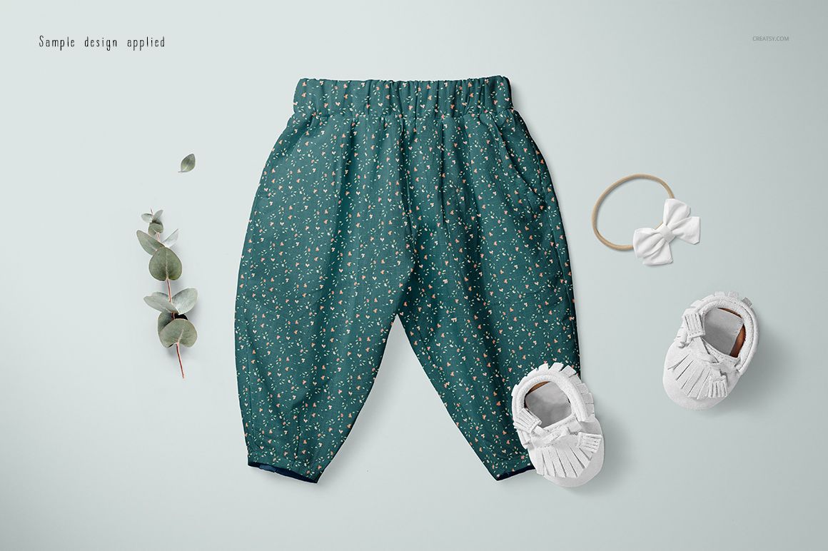 PSD mockup of baby lantern harem pants in green with tiny floral prints, shown with baby shoes and a bow headband.