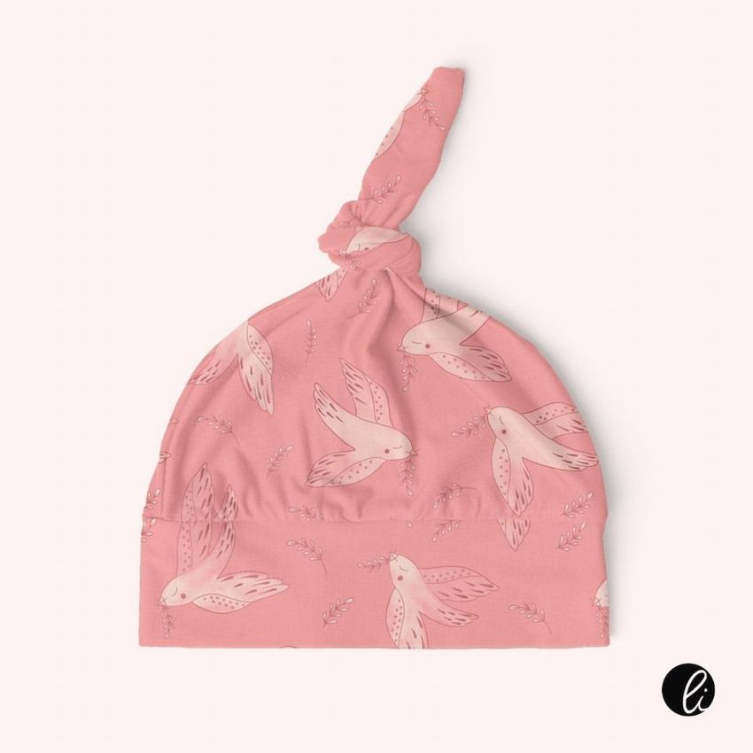 Swaddle set mockup featuring a pink baby hat with a top knot, decorated with a repeating bird and leaf pattern on a light background.