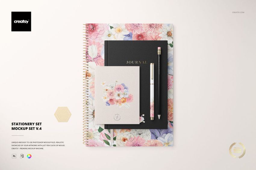 Top view of a stationery set mockup featuring a floral spiral notebook, black journal, pen, and floral card on a light background.