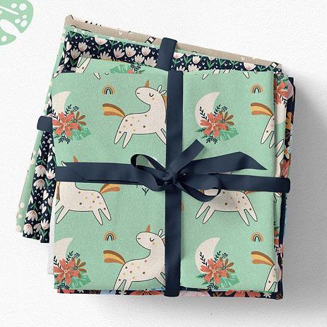 Fabric stack mockup featuring folded textiles with playful unicorn and floral patterns, tied with a dark ribbon on a light surface.