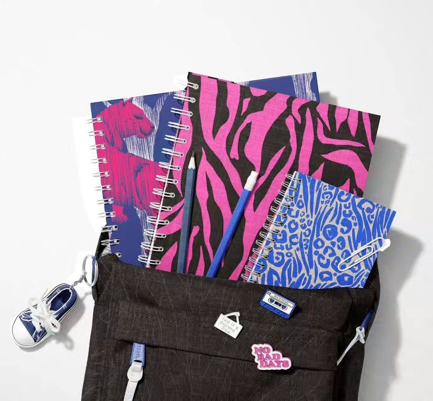 School backpack mockup with spiral notebooks featuring bold animal print covers in pink, purple, and blue, viewed from above.