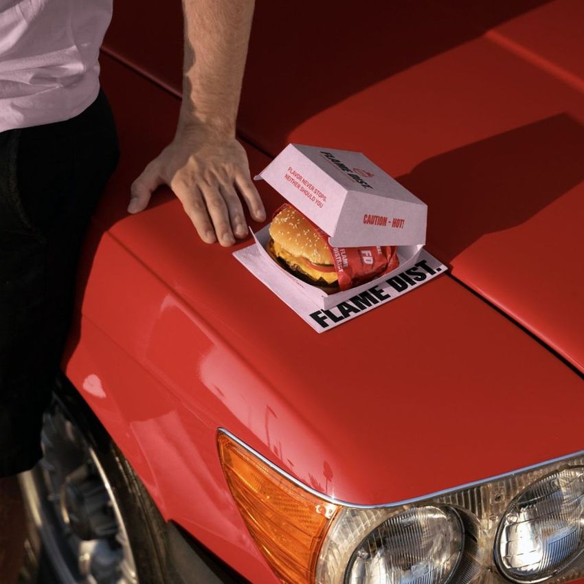 Burger packaging mockup featuring a burger in a branded box placed on the hood of a red car, with a person's hand nearby.