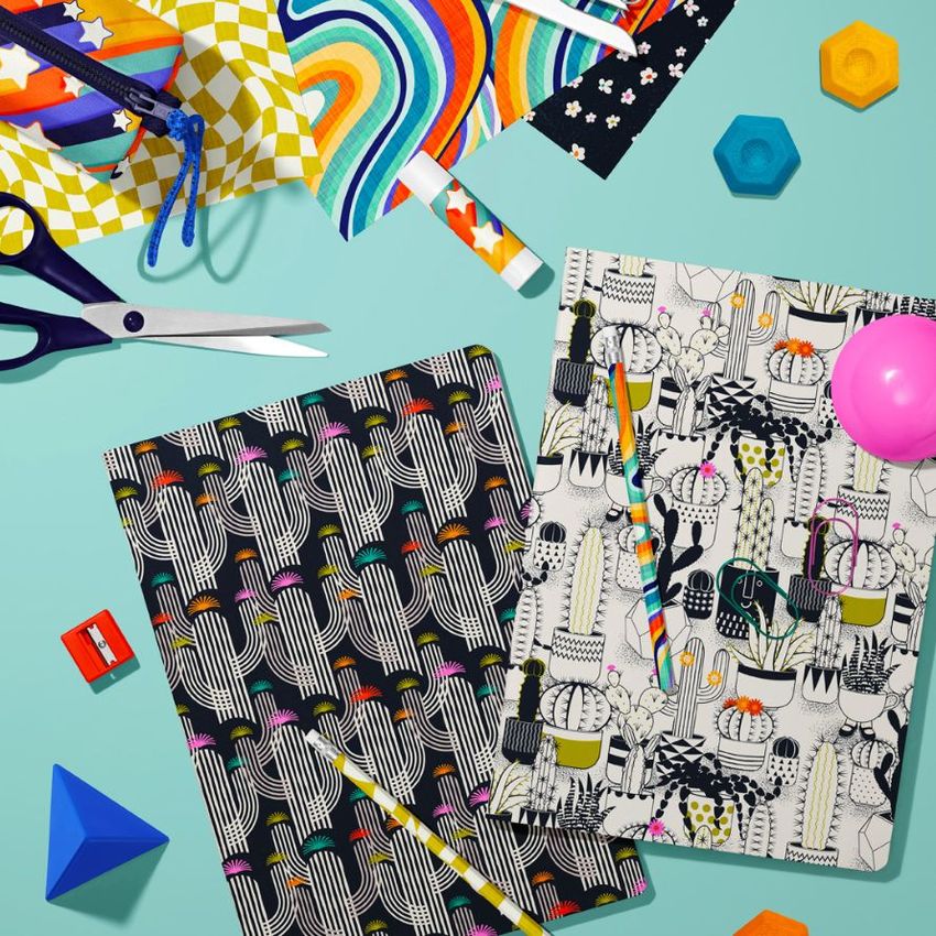 Stationery mockup featuring two classic A4 notebooks with bold cactus patterns, surrounded by colorful office supplies on a light blue surface.