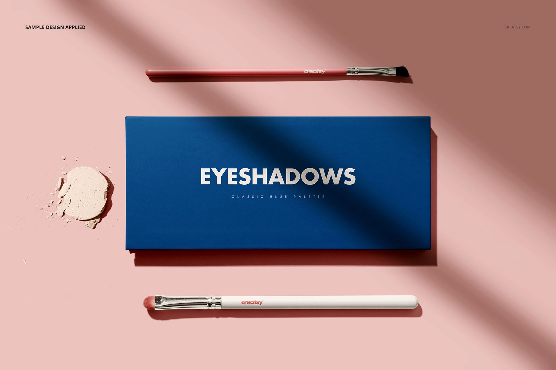Eyeshadow palette mockup with a blue rectangular case, two makeup brushes, and powder on a pink background, top view.