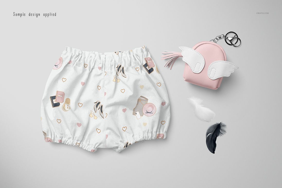 Baby harem shorts mockup featuring a whimsical print, shown alongside a small pink pouch with white wings and loose feathers.