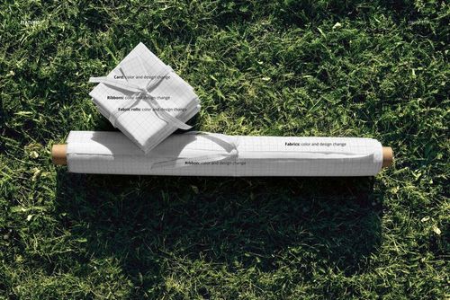 PSD mockup featuring a fabric roll and folded fabric squares with subtle grid design, placed outdoors on grass.