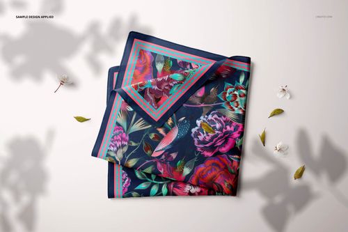 Folded square silk scarf mockup with colorful botanical and bird motifs, shown from a top view with soft shadows.