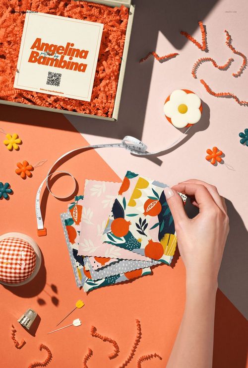 Top view of a hand arranging colorful jersey fabric swatches with floral and abstract patterns on an orange surface.
