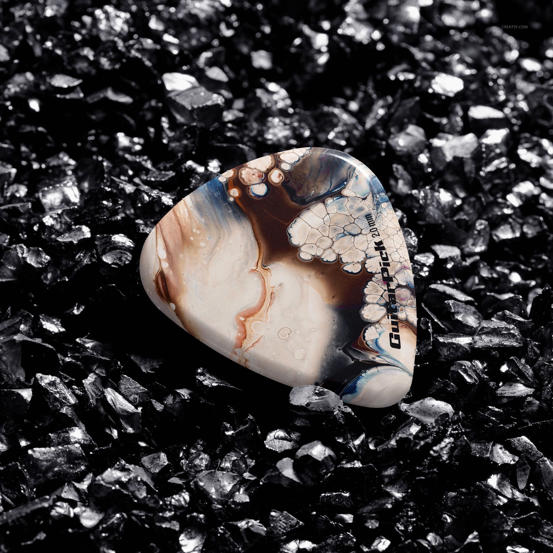 Marbled guitar pick placed on glossy black gravel, highlighting texture and detail in a high-resolution mockup scene.