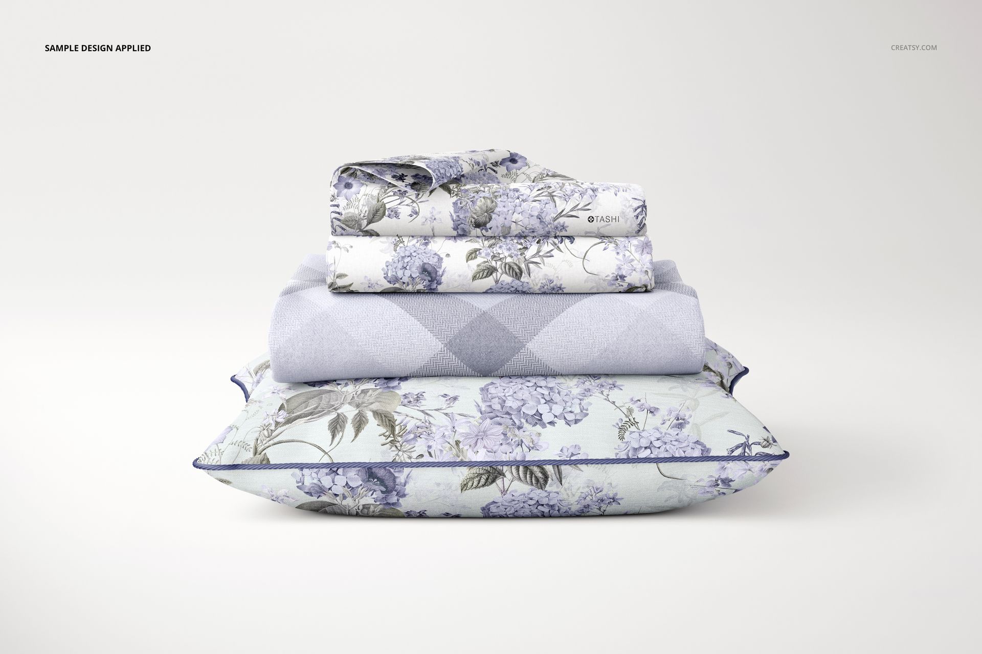 Front view of a PSD mockup featuring a braided pillow, blanket, and pillowcases in pastel blue floral and argyle designs.
