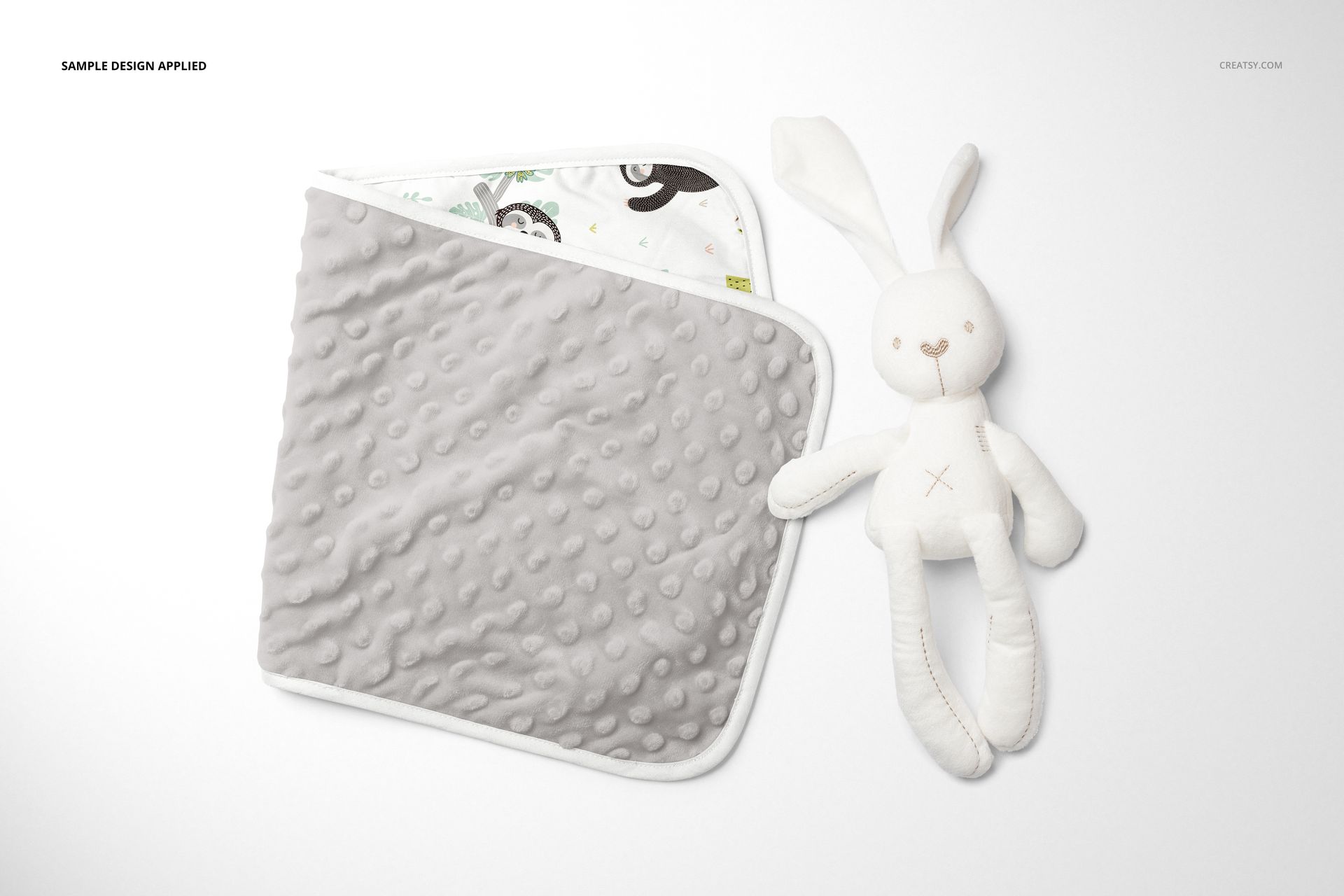 PSD mockup of a kids burp cloth in light gray with raised dots, paired with a stuffed bunny on a clean white surface.