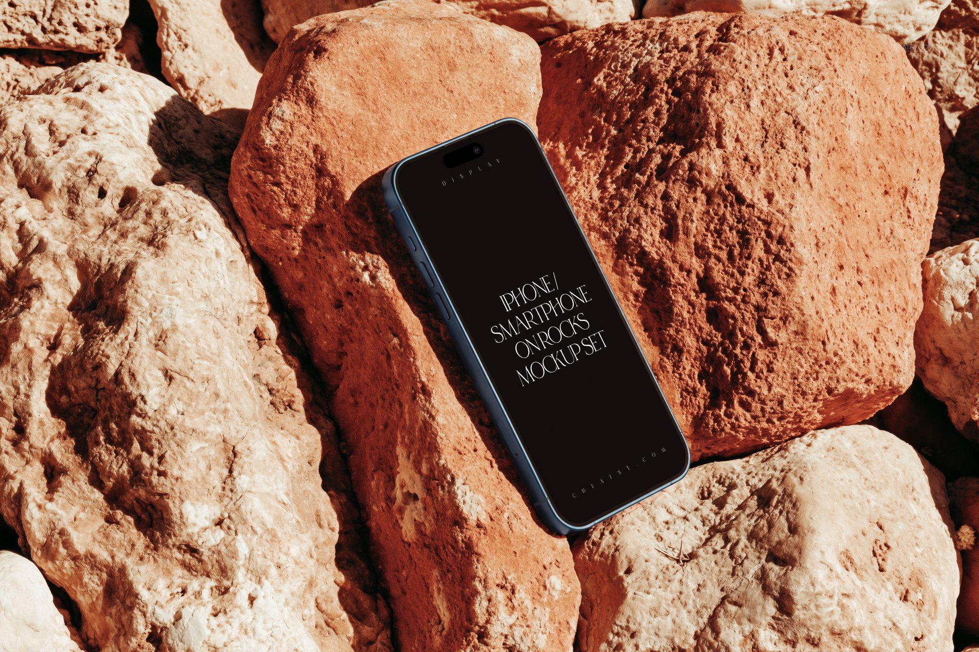 PSD mockup of an iPhone smartphone resting on rough, reddish rocks, shown from a slightly tilted perspective.