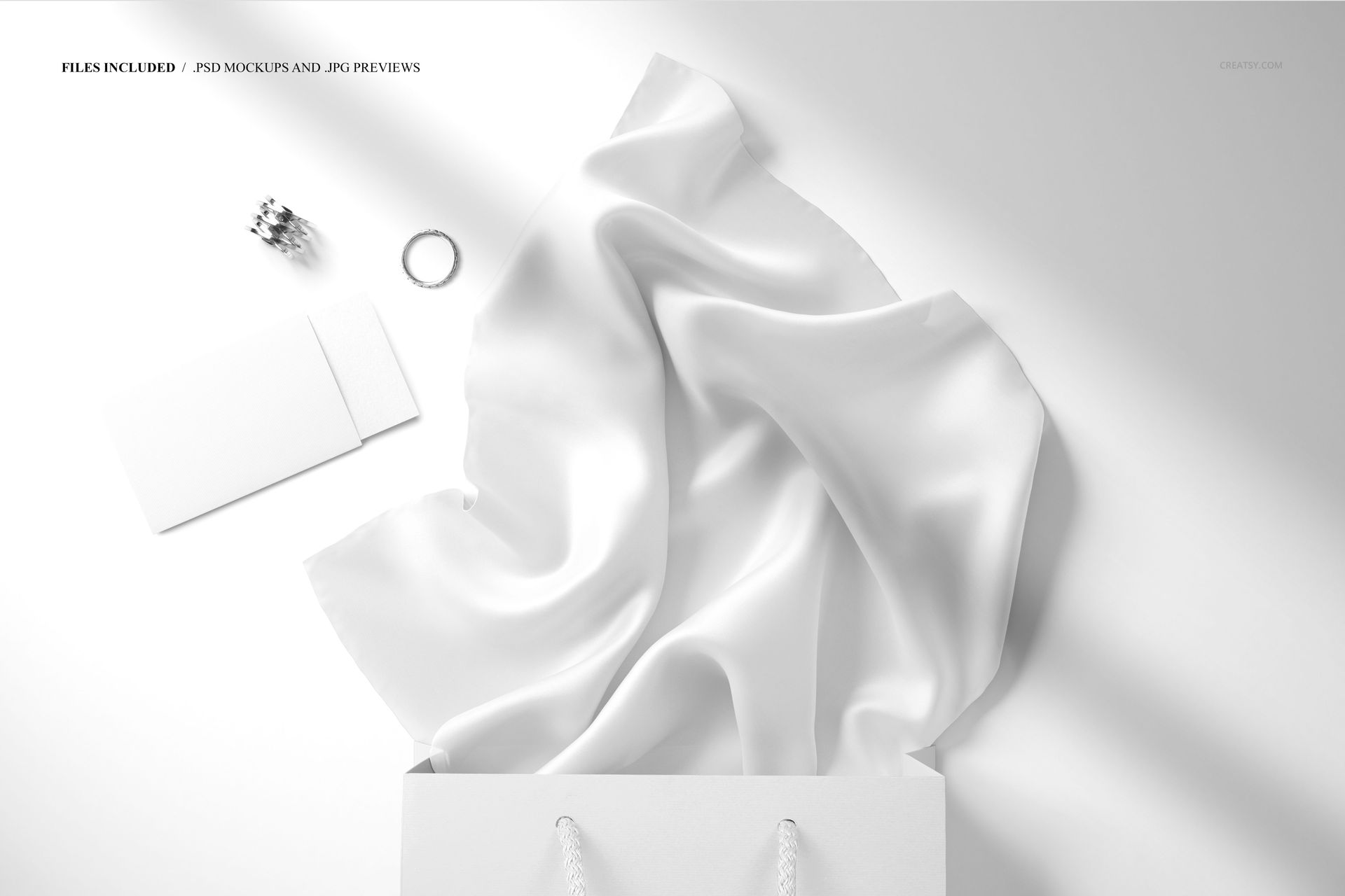 Silk scarf mockup featuring a smooth white fabric flowing out of a gift bag, with jewelry and a card nearby on a white background.
