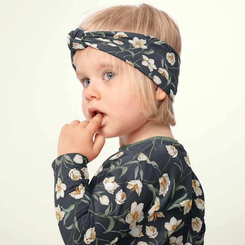 Young child in profile dressed in a dark floral-patterned headband mockup and shirt, standing before a plain backdrop.