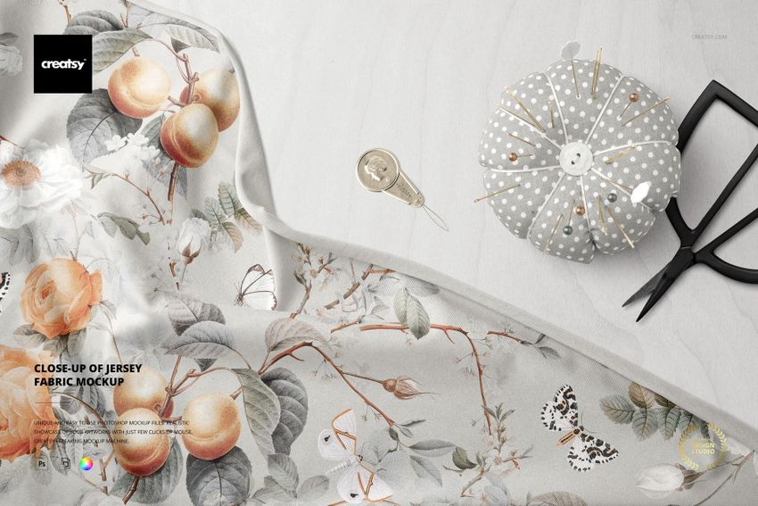 Close-up view of jersey fabric mockup with a floral and fruit pattern, next to sewing tools on a light surface.