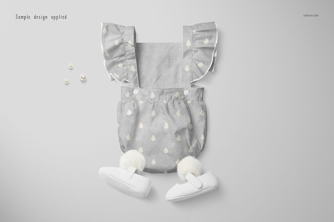 Front view of a baby romper mockup with ruffled shoulder straps, light gray fabric, and white teardrop pattern on a plain background.