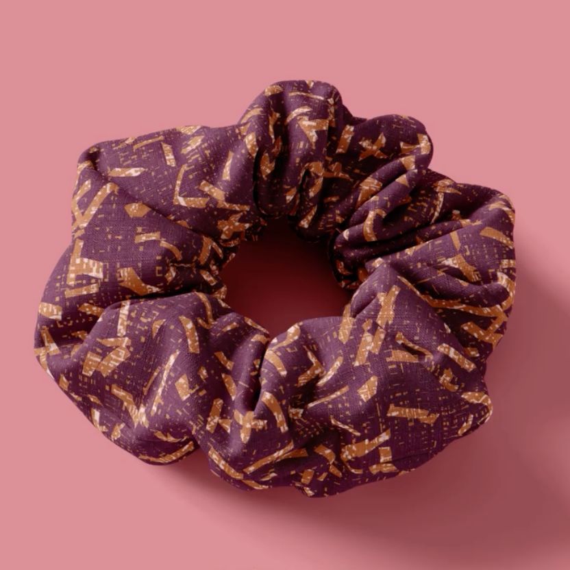 Purple and gold patterned hair scrunchie mockup displayed on a solid pink background with soft shadows.