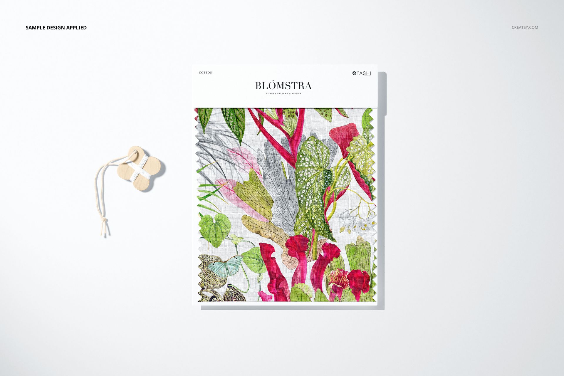 Square fabric swatch mockup with vibrant leaf and flower design, displayed on a clean surface next to wooden thread winders.