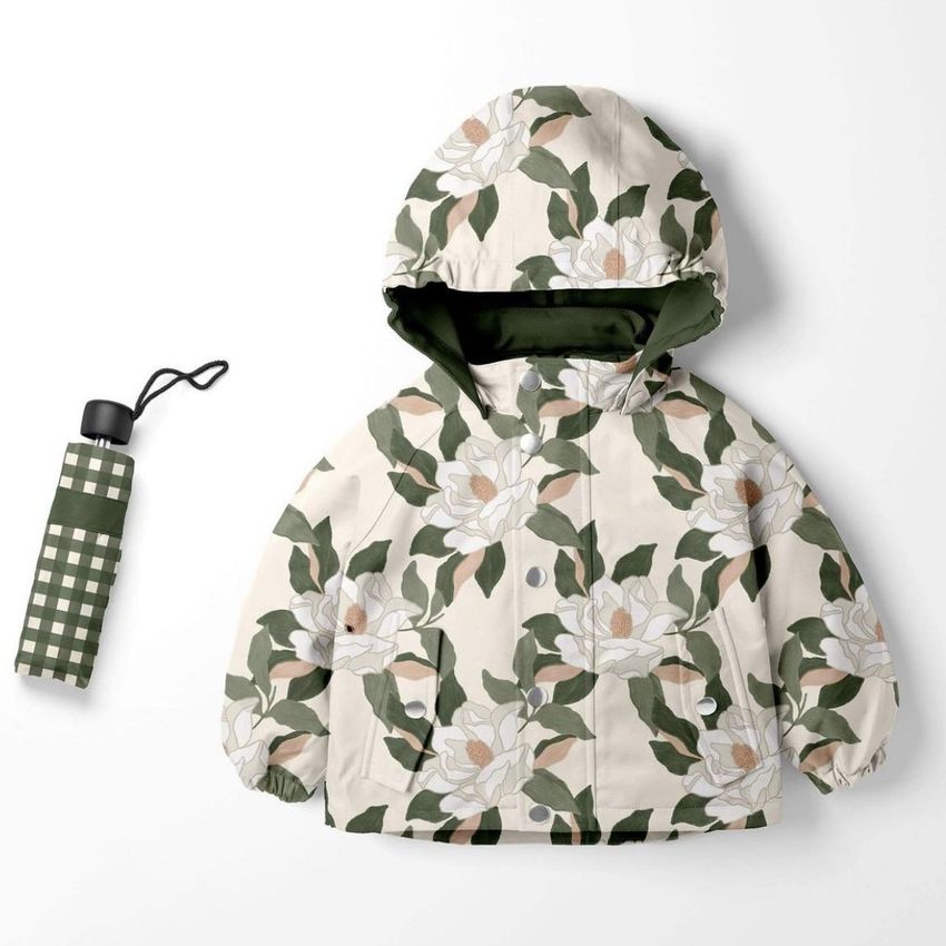 Kids rainwear mockup featuring a hooded jacket with a large green and white floral pattern, displayed next to a green plaid umbrella on a white background.