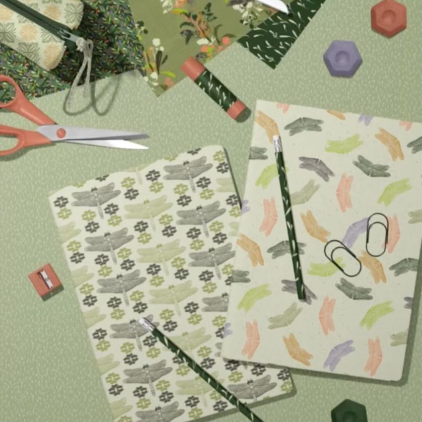 Stationery mockup featuring two classic A4 notebooks with patterned covers, pencils, scissors, and paper clips on a green surface.