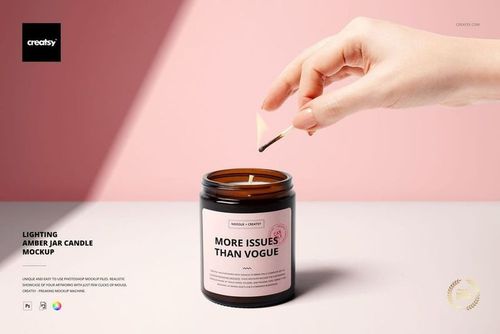 Amber glass jar candle mockup with a visible label, being lit by a hand holding a burning match, pink backdrop.
