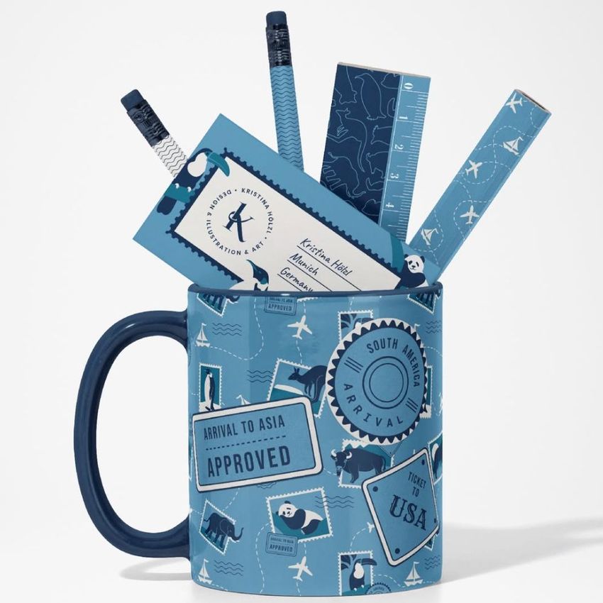 Mug mockup featuring a blue mug decorated with travel-themed stamps and labels, filled with blue office supplies on a white background.