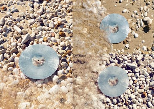 Colored vinyl record mockup set on a sunlit pebbled shore, partially touched by gentle waves and wet sand.