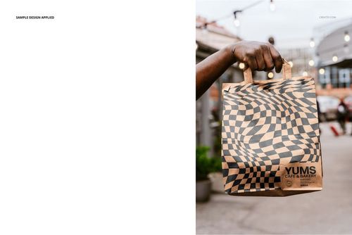 Front view of a patterned paper bag mockup with handles, shown outside with string lights and urban background.