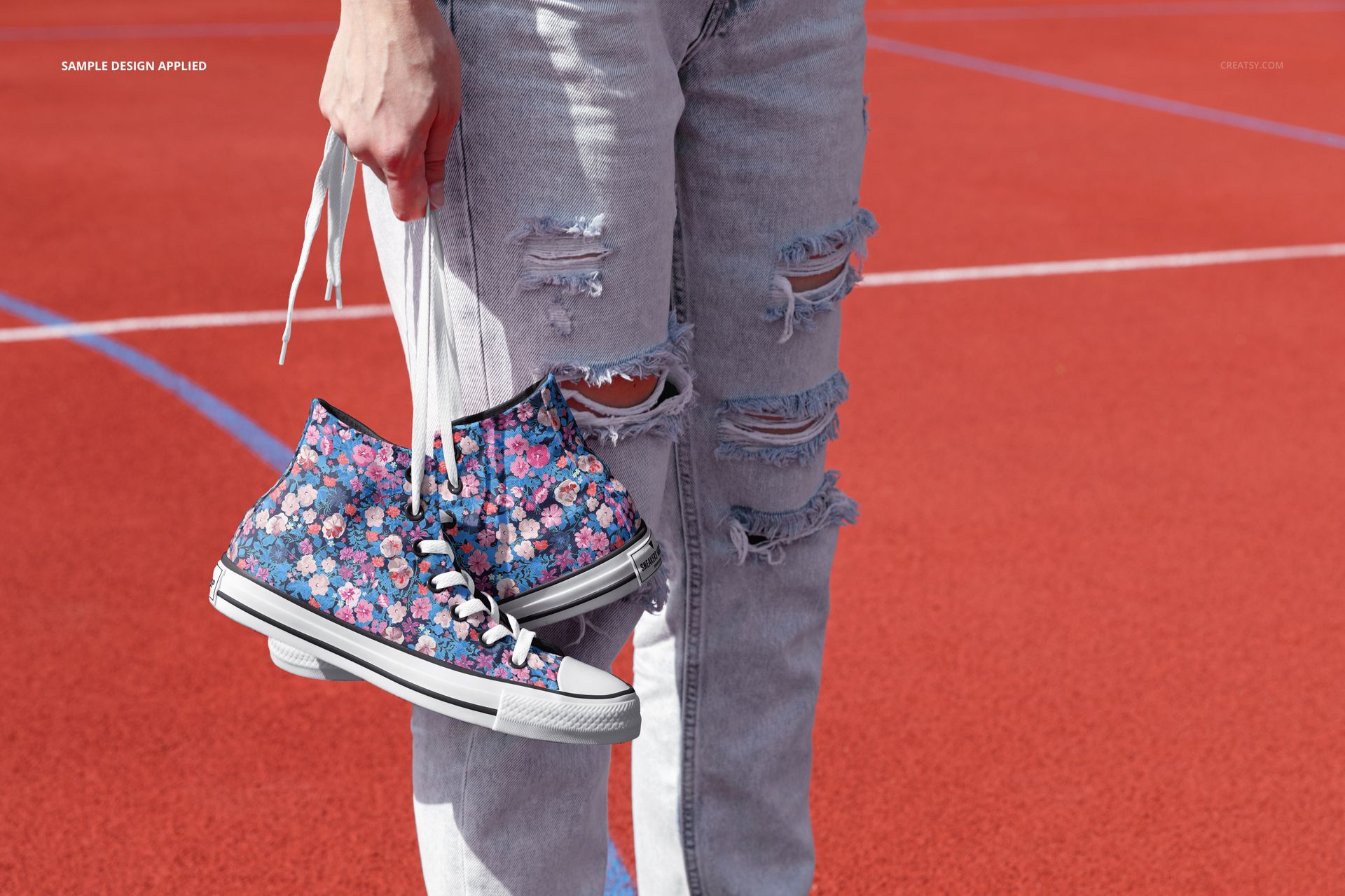 PSD mockup featuring sneakers with a colorful flower pattern, held by a person wearing distressed light jeans outdoors.