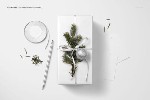 Christmas gift packaging mockup featuring white wrapping paper, ribbon, fir branches, and a metallic ornament from above.
