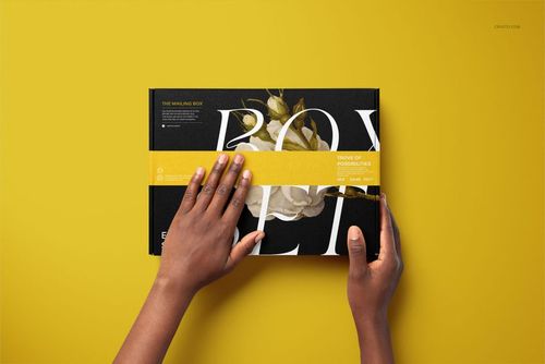 PSD mockup of a packaging box with bold text and floral print, held by hands, seen from above on yellow.