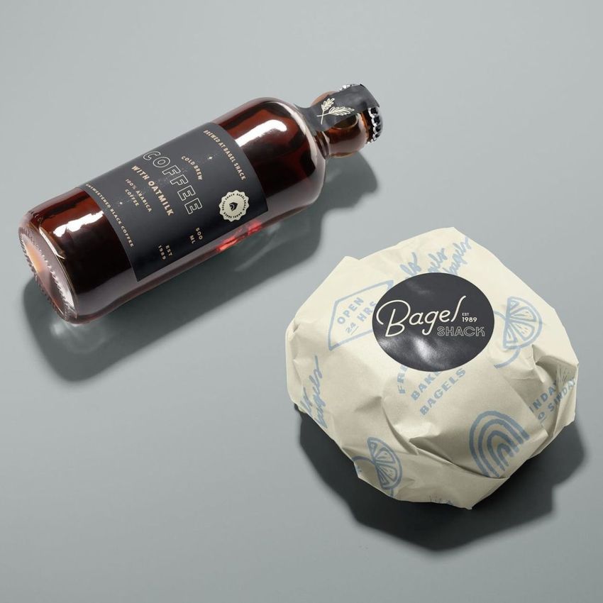 Packaging and wrapping mockup featuring a wrapped burger with a round black label and a bottle of coffee on a gray surface.