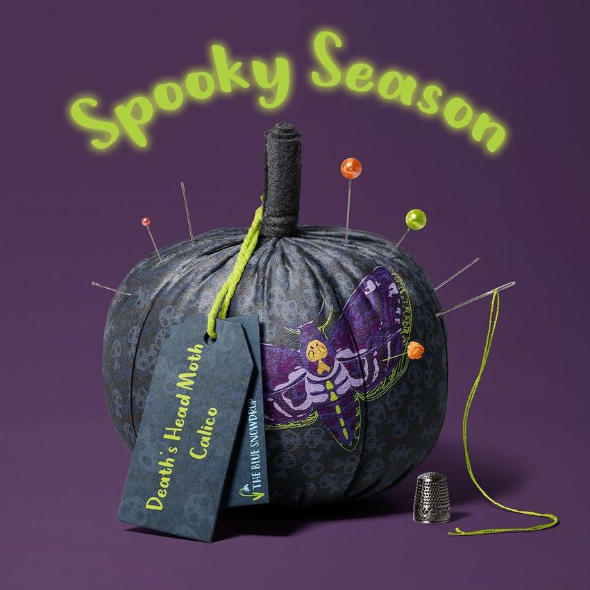 Fabric pumpkin mockup featuring a dark patterned pumpkin with a colorful moth illustration, sewing pins, and a thread spool on a purple background.