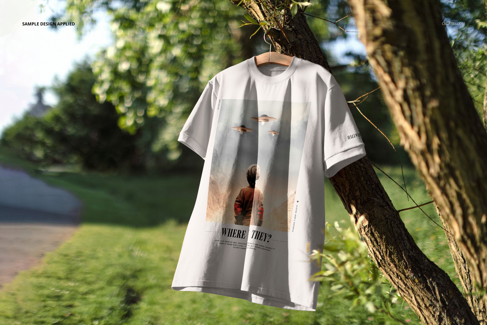 Front view of an oversized t-shirt mockup with a graphic design, displayed on a tree branch in a green park setting.